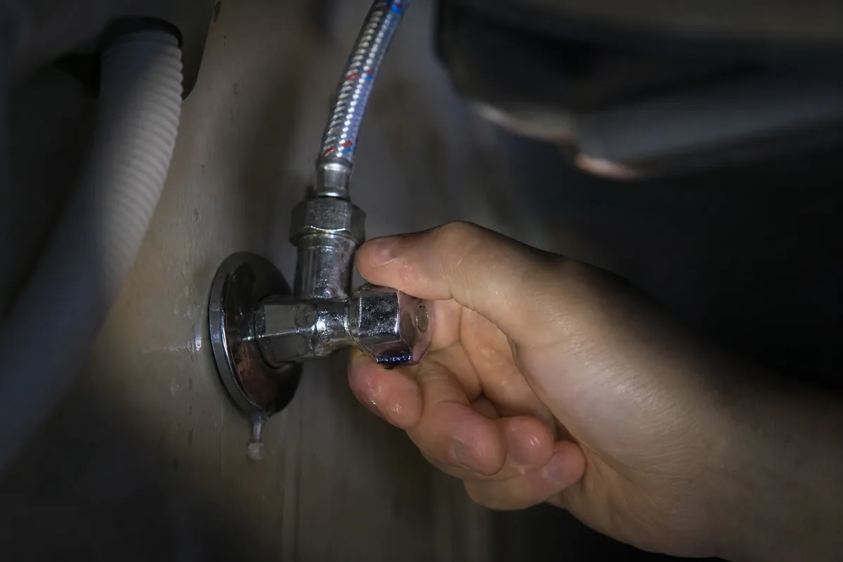 Intervention nocturne, coupure d&rsquo;eau au robinet d&rsquo;arrêt général sous un évier, lumière de lampe technique contrastée